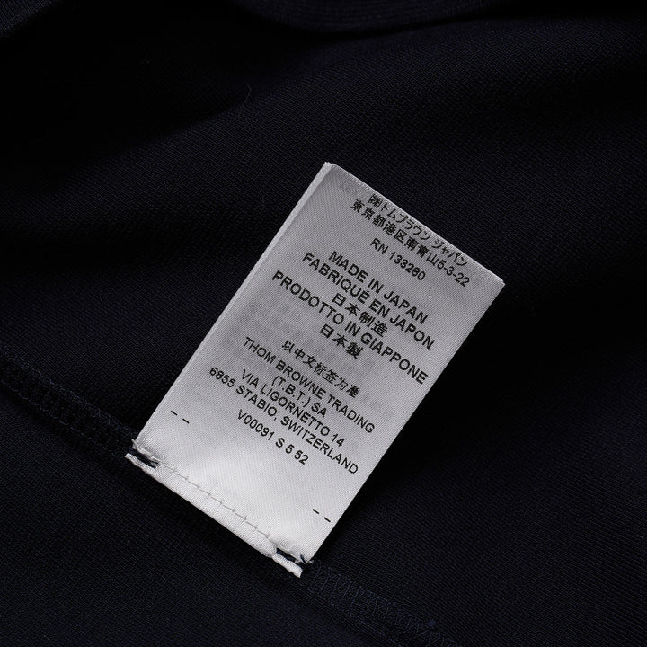 Thom Browne navy short sleeve polo with tonal 4-bar stripe on the sleeve, button placket, and woven brand label at the hem