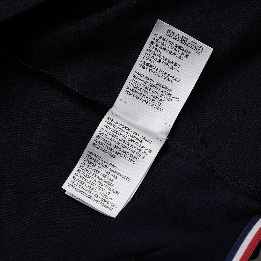 Thom Browne navy short sleeve polo with tonal 4-bar stripe on the sleeve, button placket, and woven brand label at the hem