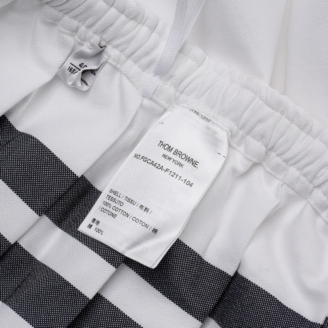 Thom Browne white mini pleated skirt with elasticated drawstring waistband and four-bar grey stripe detail on the hip, featuring a woven brand label