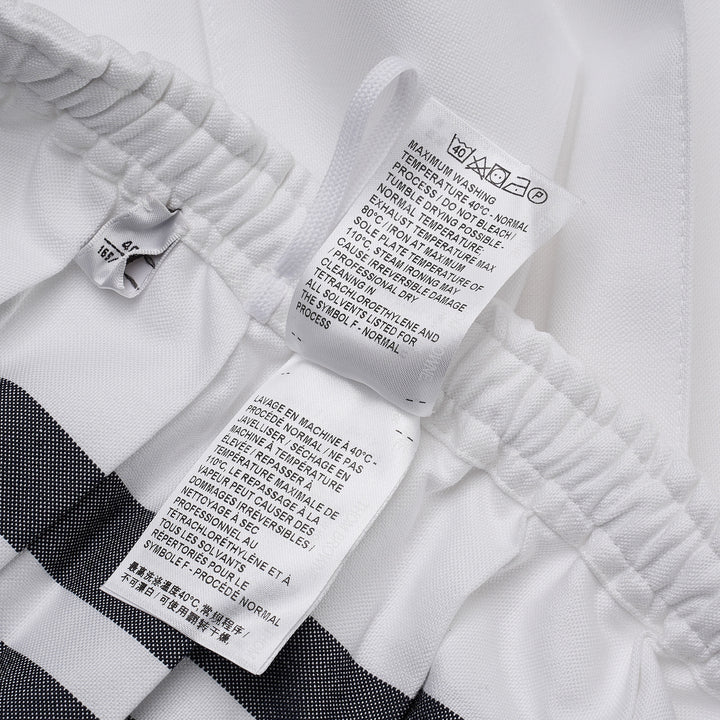 Thom Browne white mini pleated skirt with elasticated drawstring waistband and four-bar grey stripe detail on the hip, featuring a woven brand label
