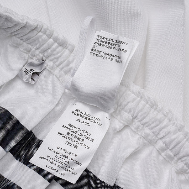 Thom Browne white mini pleated skirt with elasticated drawstring waistband and four-bar grey stripe detail on the hip, featuring a woven brand label