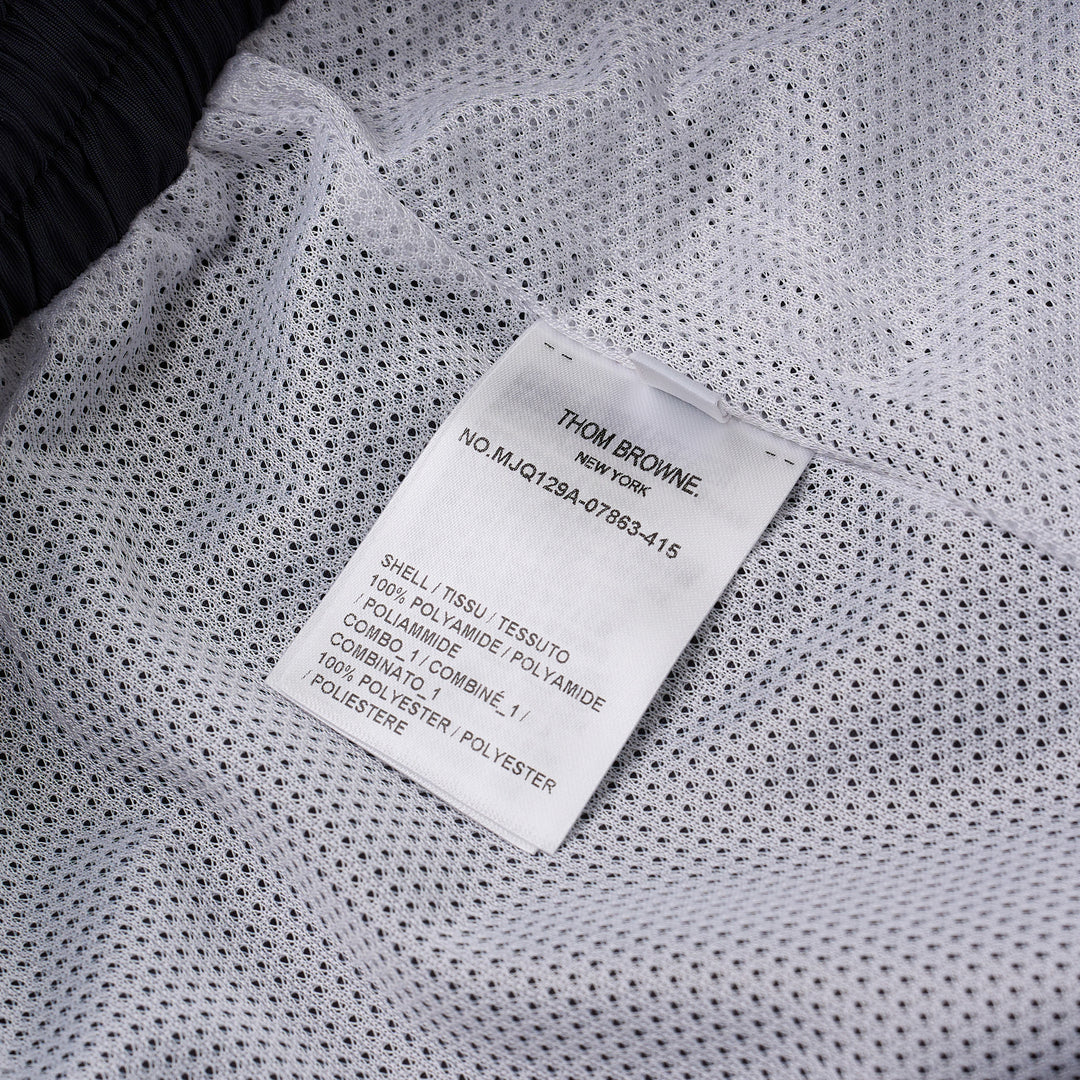 Thom Browne navy track pants with white four-bar mesh stripe on the thigh, elasticated drawstring waist, zip pockets, and ankle toggle ties