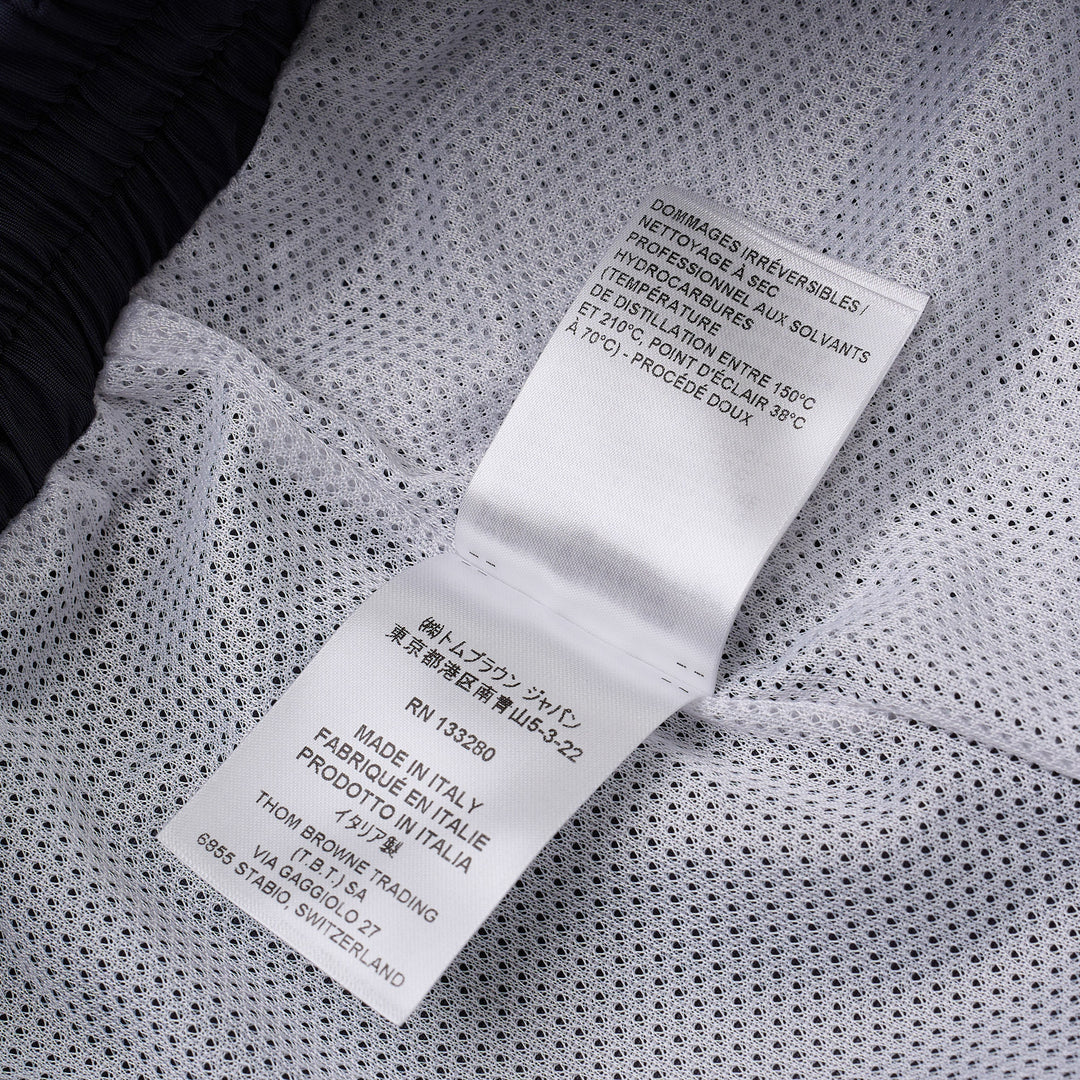 Thom Browne navy track pants with white four-bar mesh stripe on the thigh, elasticated drawstring waist, zip pockets, and ankle toggle ties