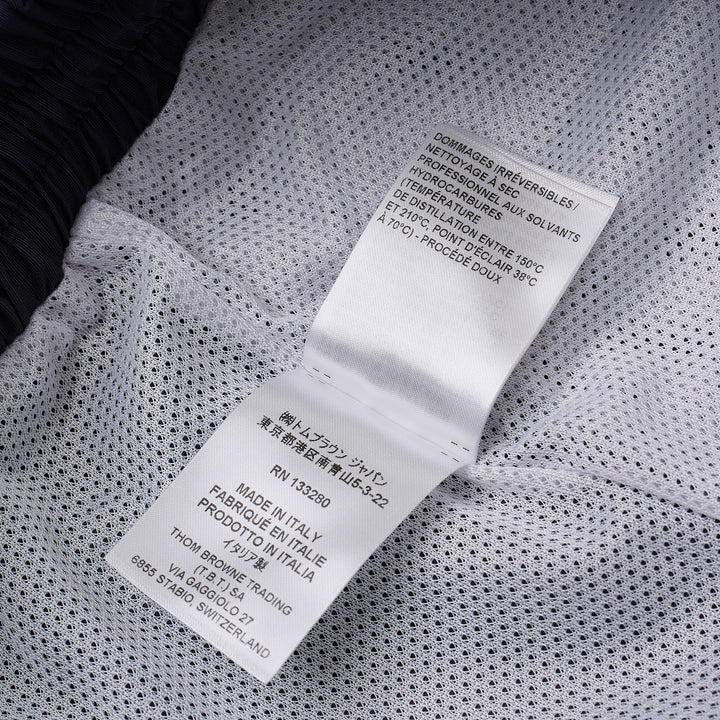 Thom Browne navy track pants with white four-bar mesh stripe on the thigh, elasticated drawstring waist, zip pockets, and ankle toggle ties