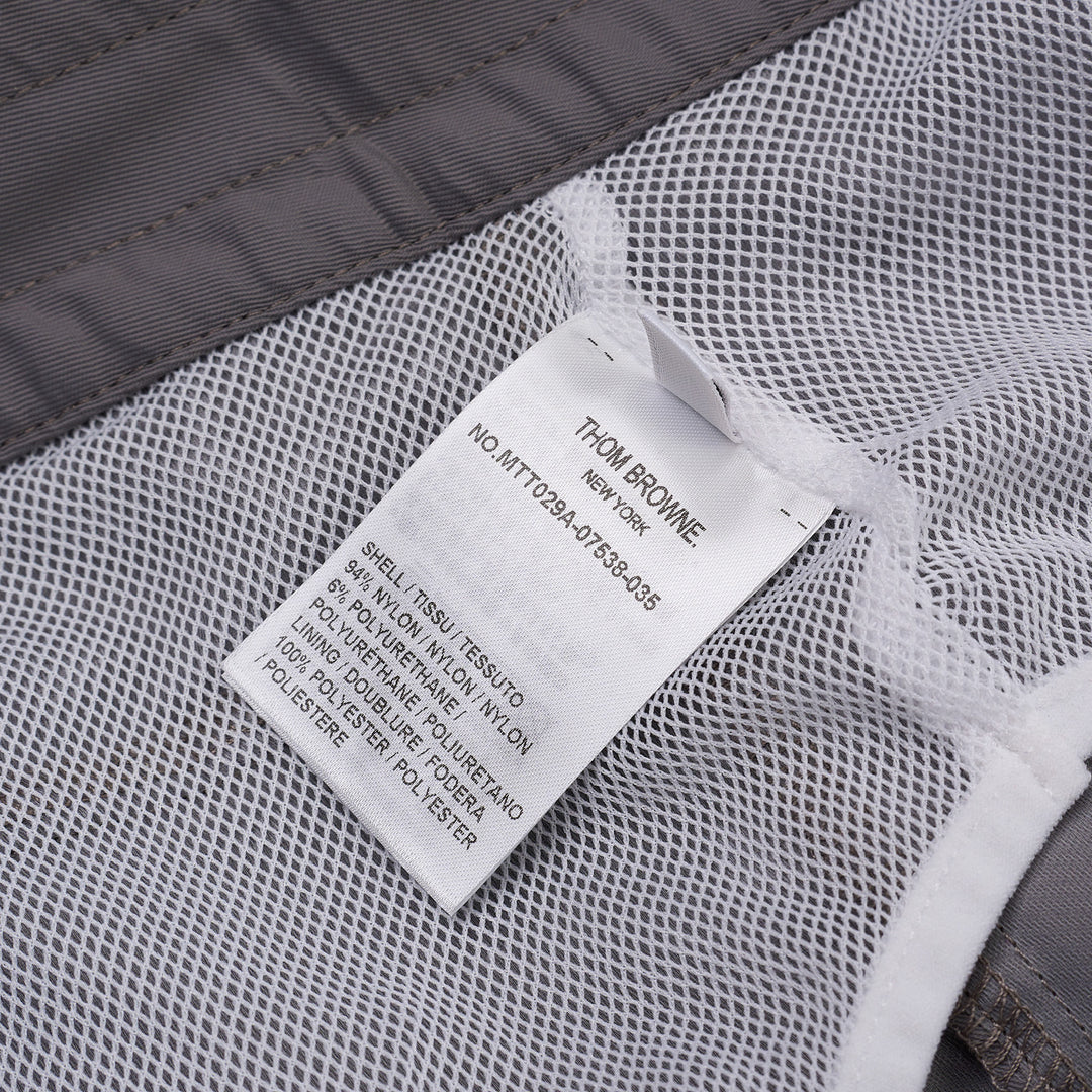 Thom Browne grey board shorts with 4-bar white stripe detail on one leg, red and white braided drawstring waist, and woven logo label at the hem