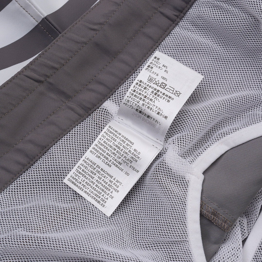 Thom Browne grey board shorts with 4-bar white stripe detail on one leg, red and white braided drawstring waist, and woven logo label at the hem