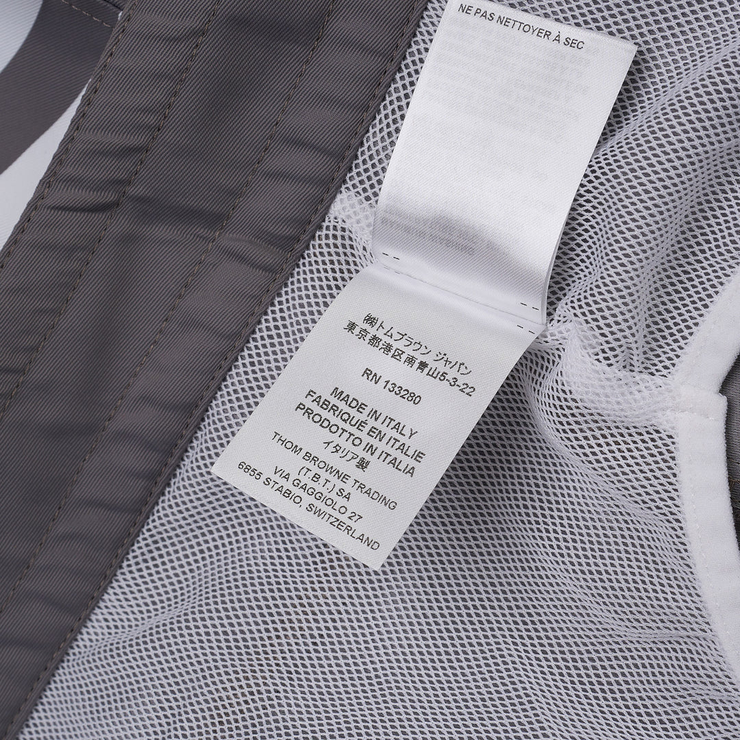 Thom Browne grey board shorts with 4-bar white stripe detail on one leg, red and white braided drawstring waist, and woven logo label at the hem