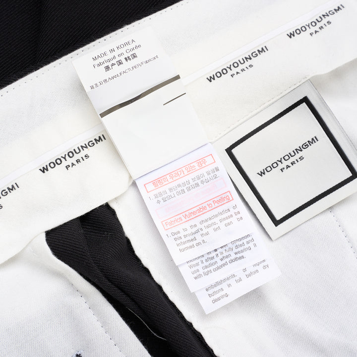 Wooyoungmi black pleated high-rise trousers with double front pleats and side metal buckle adjuster, displayed flat on white background - view 5