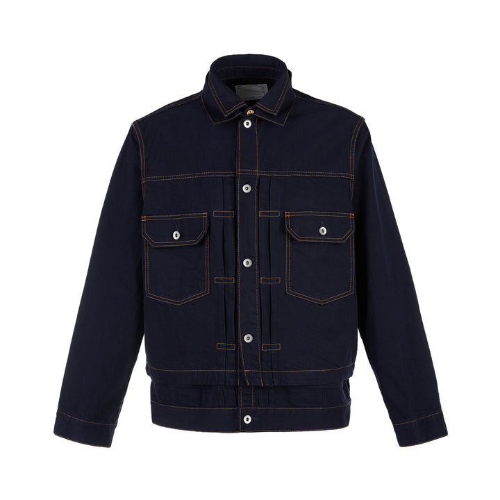 sacai indigo denim trucker jacket with contrast topstitching, pleated front panels, button-flap chest pockets and a layered hem, shown from the front