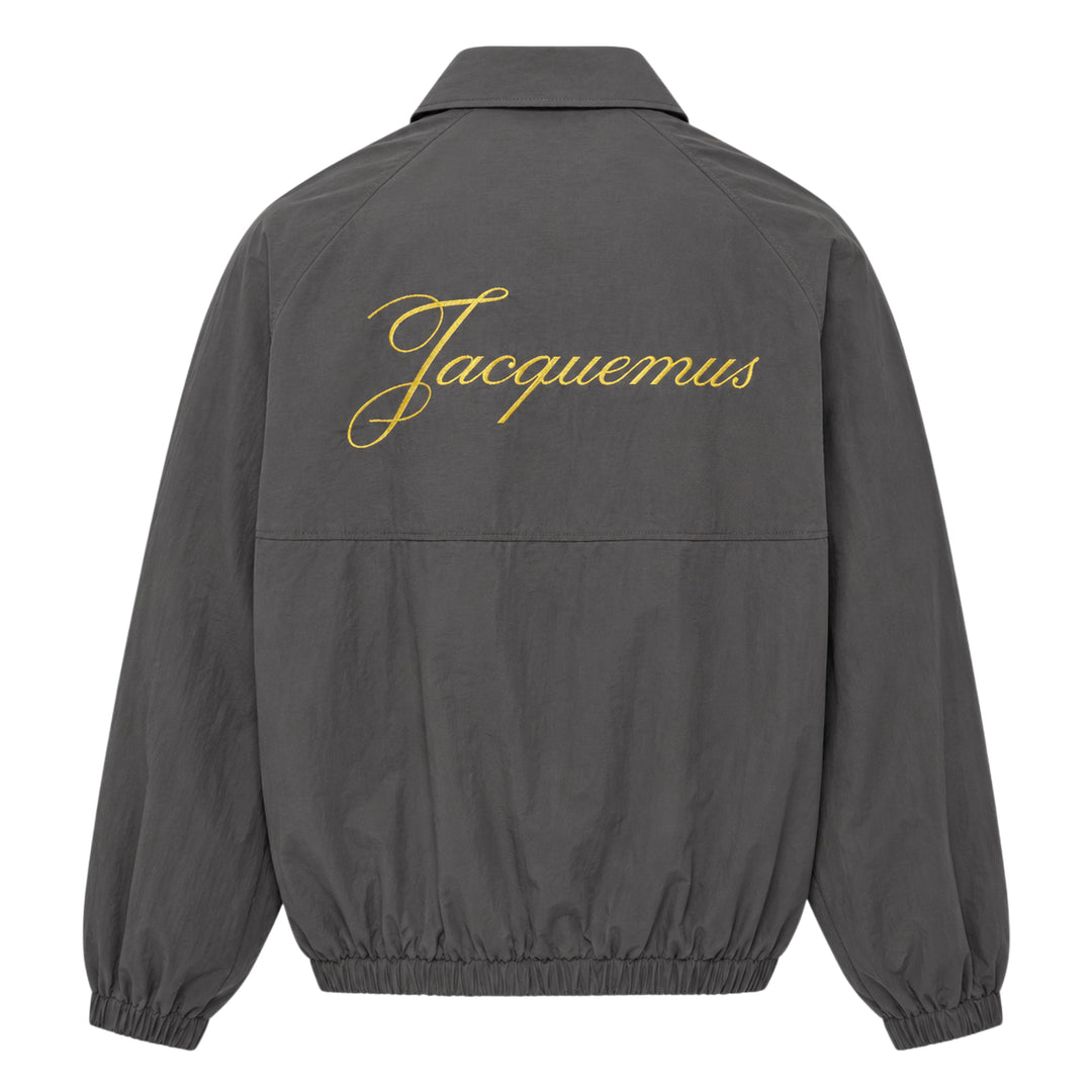 Jacquemus Le Coupe-Vent blouson in slate grey with full-length zip closure, gold script 'J' embroidery on the chest, elasticated cuffs, and drawstring hem - view 2