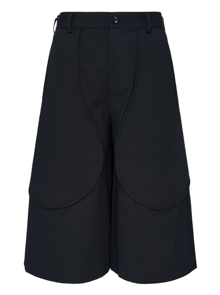 Comme des Garçons Black wool gabardine wide-leg shorts in black, featuring sculptural curved oversized patch pockets on the front panels and a high-rise tailored waistband with single button closure
