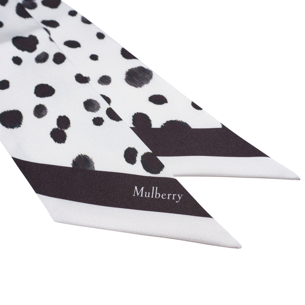 Mulberry Dalmatian Skinny Scarf in white with black brushstroke spot print and solid black branded border at one end, laid flat on a white background