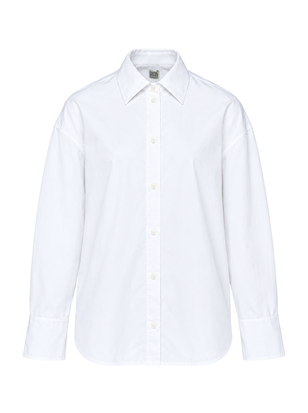 Totême Boxy Poplin Shirt in white, featuring a pointed collar with woven monogram label, full button fastening, long sleeves with barrel cuffs, and a relaxed oversized silhouette