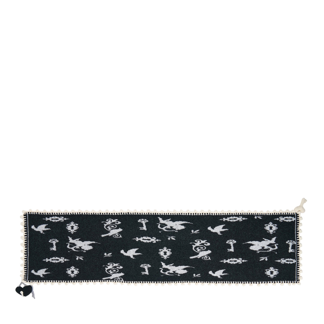 Renli Su knit long scarf in dark charcoal with allover ivory bird, key, and lock jacquard motif, finished with a hand-crocheted ivory border and a woven heart charm at the corner