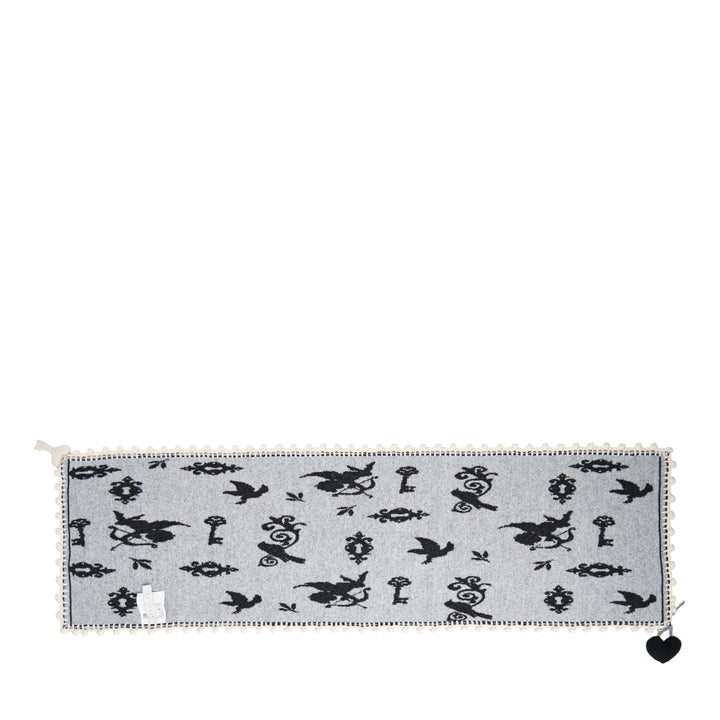 Renli Su knit long scarf in dark charcoal with allover ivory bird, key, and lock jacquard motif, finished with a hand-crocheted ivory border and a woven heart charm at the corner - view 2