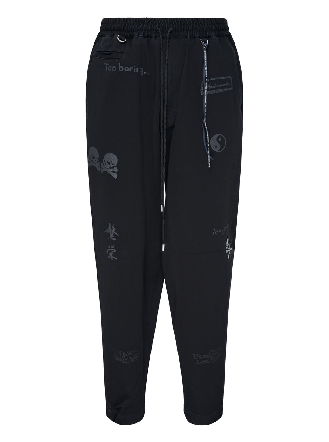Mastermind Doodle Print Easy Pants in black with all-over graphic prints including skull-and-crossbones, yin-yang symbol, kanji script, and hand-scrawled text, featuring an elasticated drawstring waistband and tapered leg