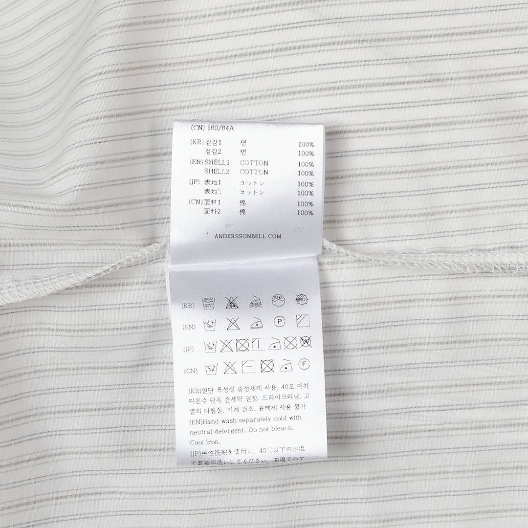 Andersson Bell Asymmetric Studded Stripe Shirt in white pinstripe with metallic stud button placket and draped asymmetric hem, flat lay on white background