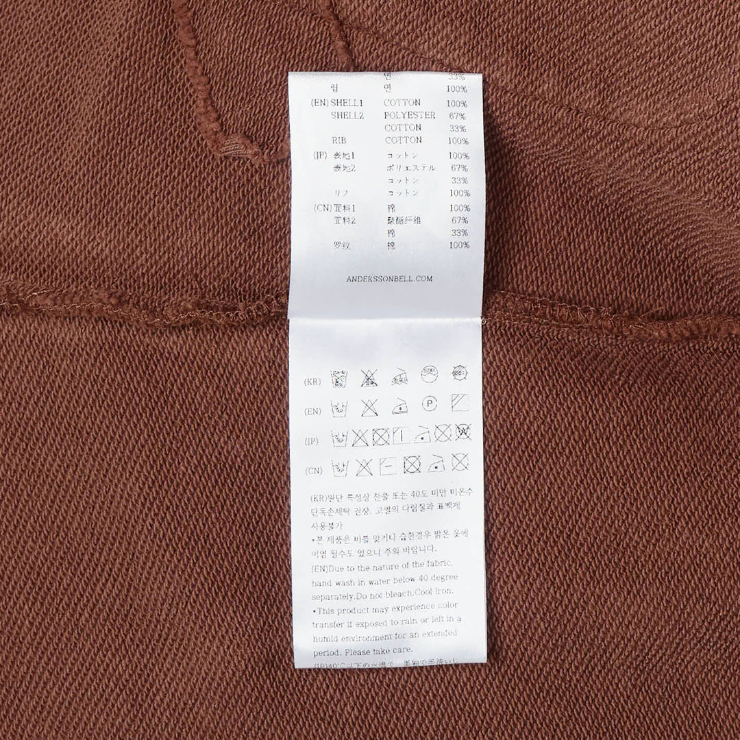 Andersson Bell Raw-Cut Studded Zip-Up Hoodie in dark brown with tonal collegiate embroidery, gunmetal-studded raw-cut pockets, and tie-detail cuffs
