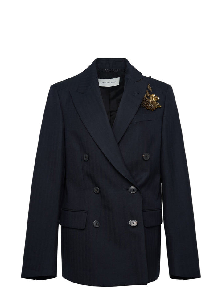 Dries Van Noten navy double-breasted blazer with peak lapels, six dark buttons, hip flap pockets, and an ornate gold embroidered brooch detail on the chest