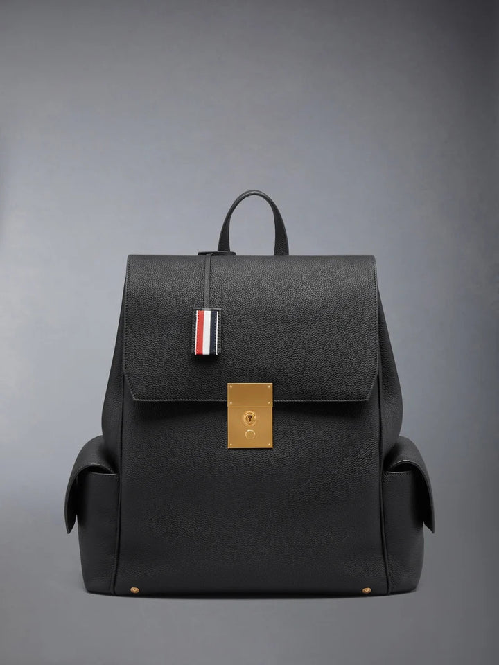 Thom Browne Bolton backpack in black soft pebble leather with brass-tone lock closure, flap side pockets, and red, white, and blue tab detail