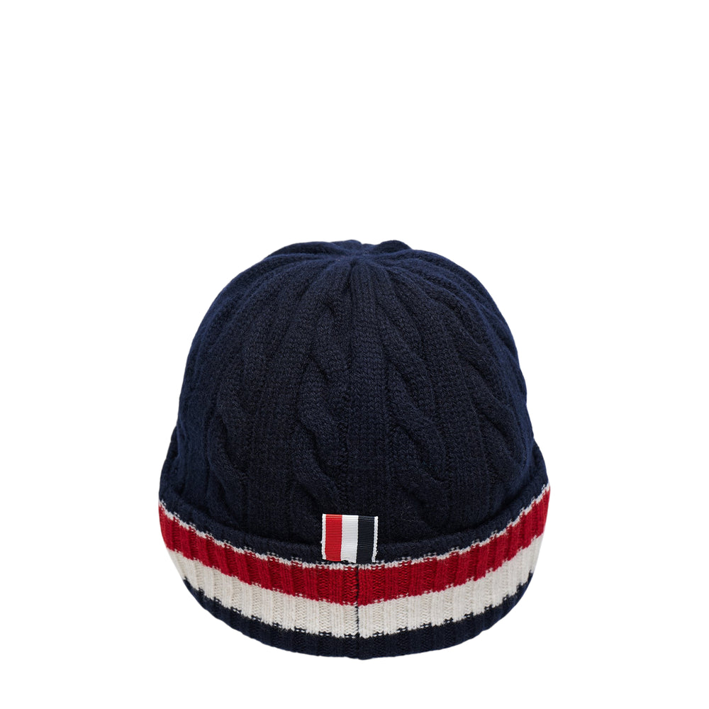 Thom Browne navy merino wool cable and rib knit beanie with signature red, white, and blue stripe detail and woven brand label at the brim, viewed from above