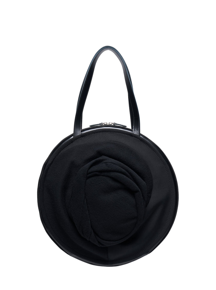 Junya Watanabe black circular top handle bag with three-dimensional draped rose appliqué on the front, leather strap, and silver-tone zip closure
