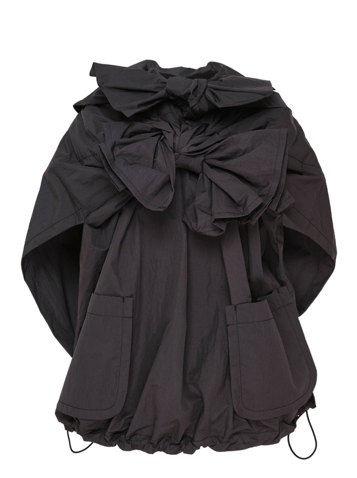 Tao structured cape top in dark charcoal with an oversized gathered bow at the neckline, patch pockets, and a drawstring elasticated hem, displayed on a plain white background