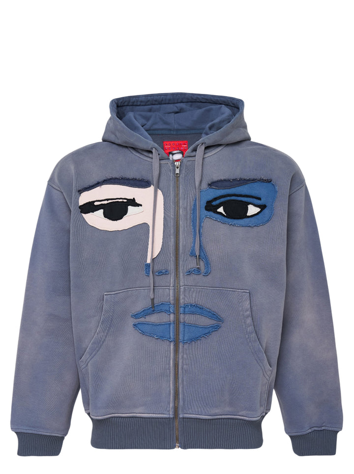 KidSuper Studios washed blue-grey zip hoodie with a patchwork appliqué face featuring mismatched eyes, nose and lips, shown from the front with drawstring hood and kangaroo pocket