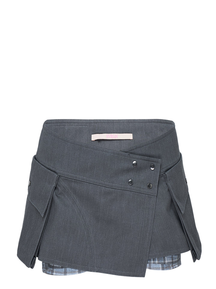 Sultry Virgin Utility Cargo Skort in grey suiting fabric, featuring a crossover wrap waistband with snap buttons, layered pleated panels, cargo pocket detailing, and a plaid underlay at the hem
