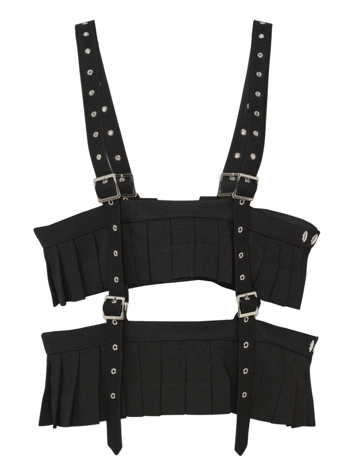 Noir Kei Ninomiya black polyester gabardine harness vest with knife-pleated panels, silver buckles, and studded shoulder straps on a white background