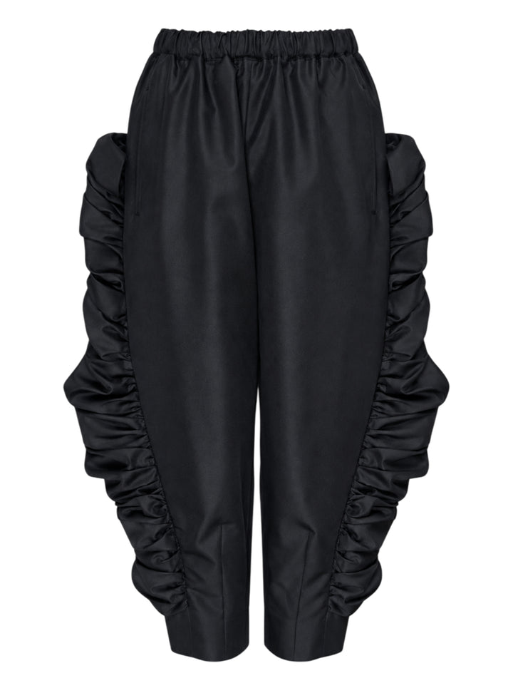 Comme des Garçons wide-leg black pants with dramatic ruched frill panels along both side seams and an elasticated waistband, displayed flat against a white background