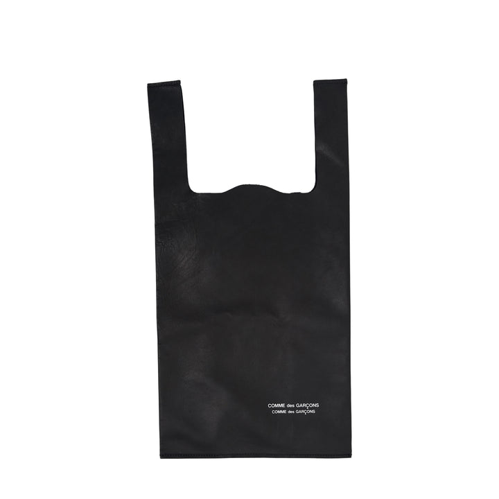 Comme des Garçons Comme des Garçons small straight-cut black leather tote bag with wide handles and logo print at base, flat lay on white background