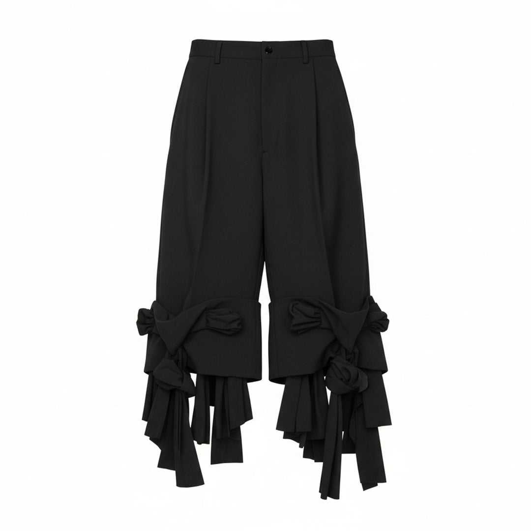 Comme des Garçons Homme Plus black wool tropical wide-leg pants with sculptural knotted bow and cascading ribbon hem trim, front view on white background