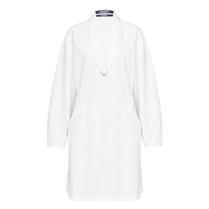 Jacquemus La Robe Colombe white long-sleeve mini dress with deep V-neckline, elasticated waist, front patch pocket, and navy logo tape at the back collar