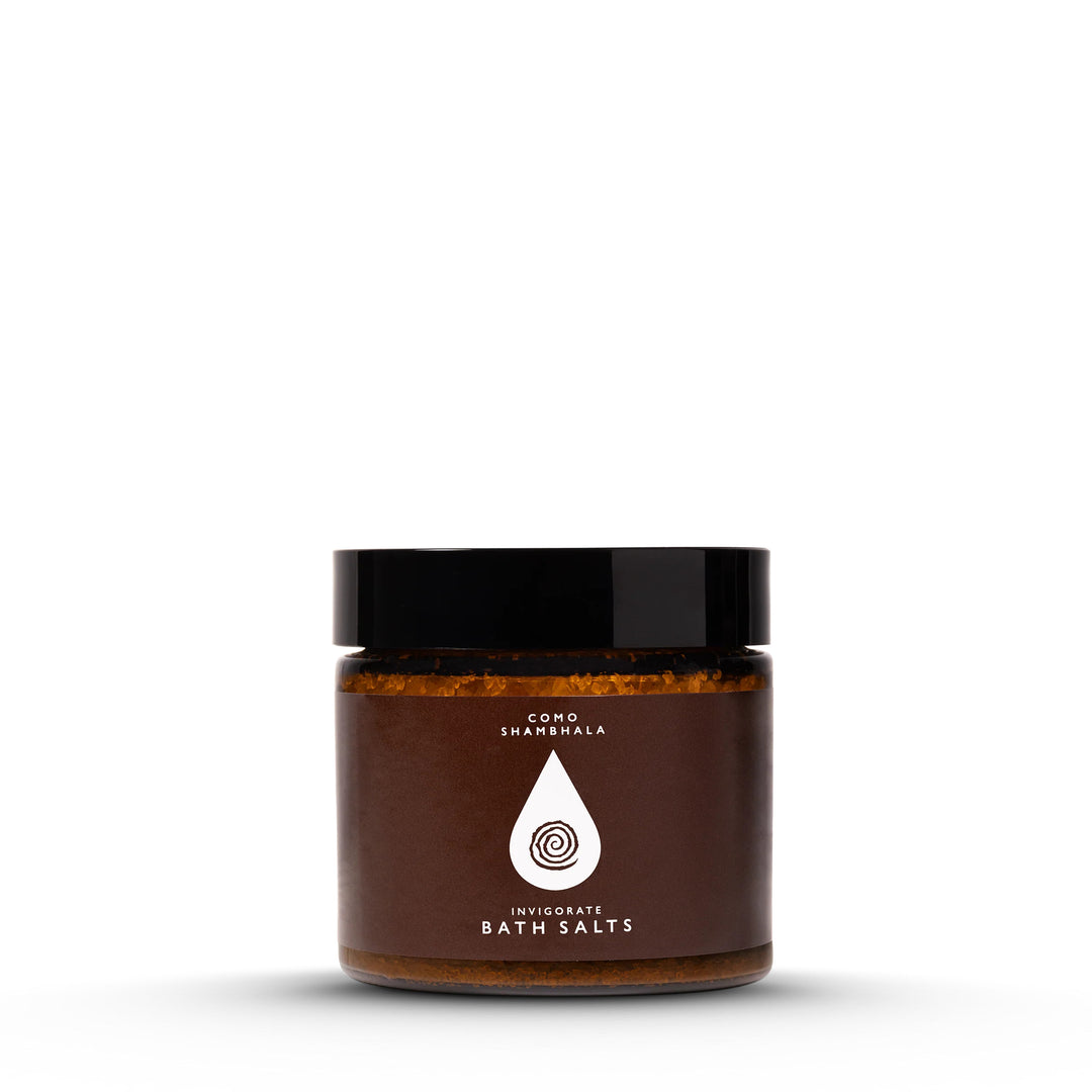 COMO Shambhala Invigorate Bath Salts in an amber jar with black lid and brown label featuring a white water-drop spiral logo