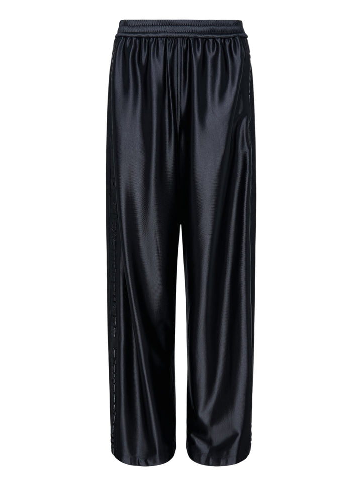 Alexander Wang mid-rise black glossy track pants with embossed side logo panels and elasticated waistband, shown from the front