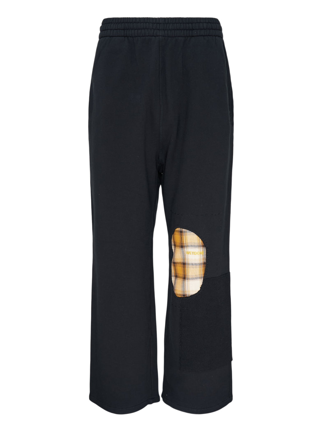 We11done Black Repaired Sweatpants with amber tartan plaid knee patch and embroidered logo, wide-leg relaxed fit, elasticated waistband, front view on white background