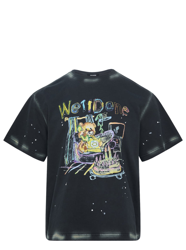 We11done Anniversary Teddy Tee in charcoal with multicolour crayon-style graphic of a teddy bear in a bumper car, paint splatter detailing, and hand-lettered We11done logo print