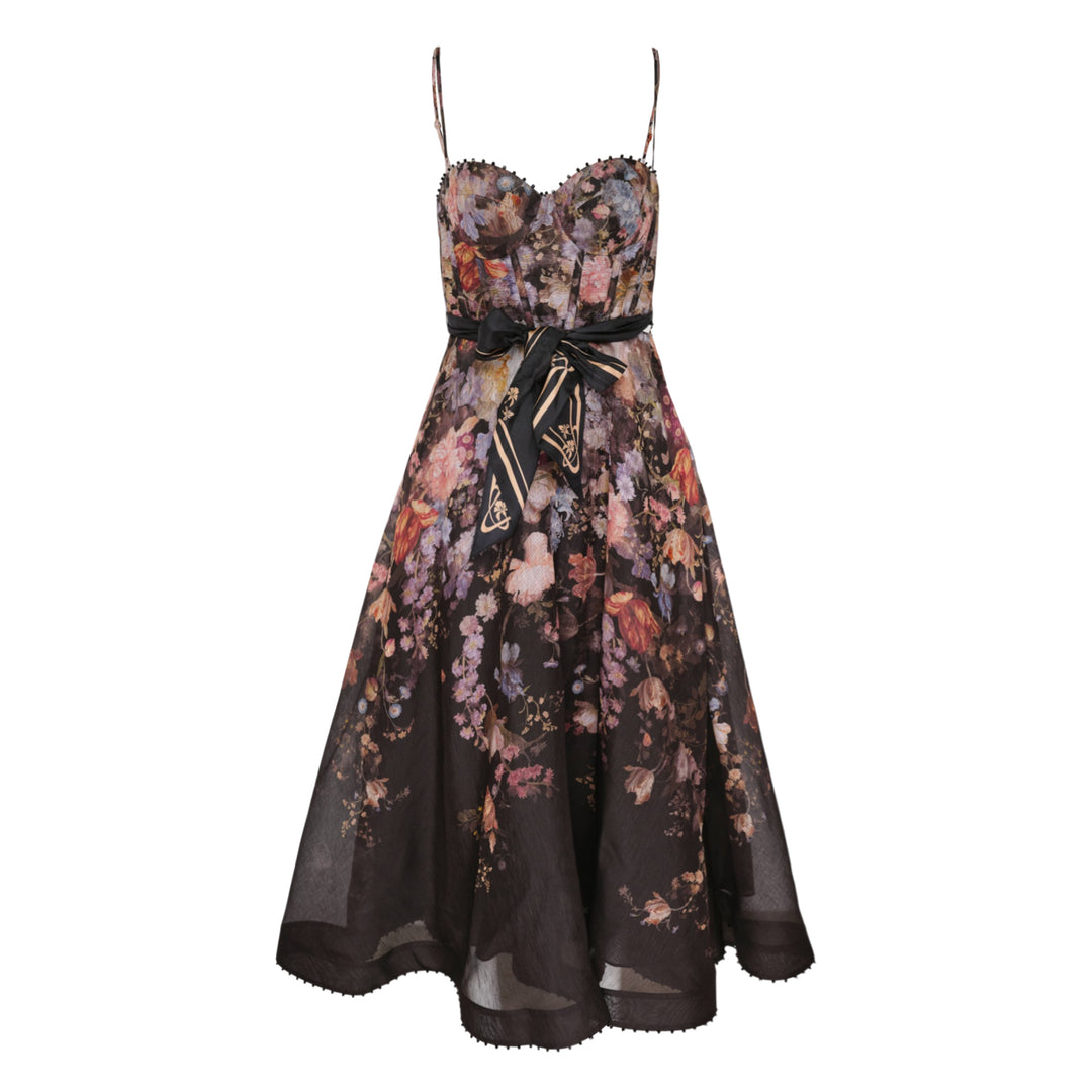 Zimmermann Valiant Corset Picnic Dress in dark botanical floral print, featuring a ruched sweetheart bodice with pom-pom trim, thin spaghetti straps, a branded satin ribbon bow at the waist, and a full semi-sheer A-line midi skirt