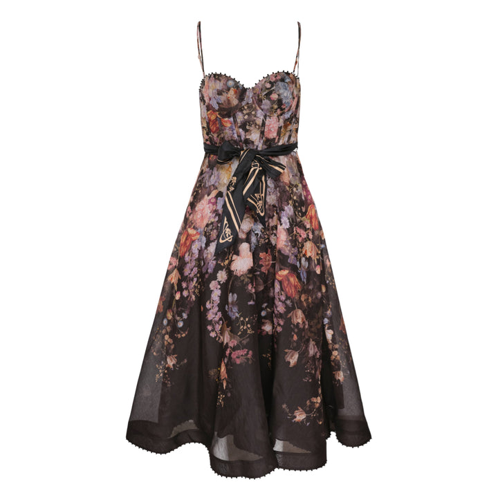 Zimmermann Valiant Corset Picnic Dress in dark botanical floral print, featuring a ruched sweetheart bodice with pom-pom trim, thin spaghetti straps, a branded satin ribbon bow at the waist, and a full semi-sheer A-line midi skirt