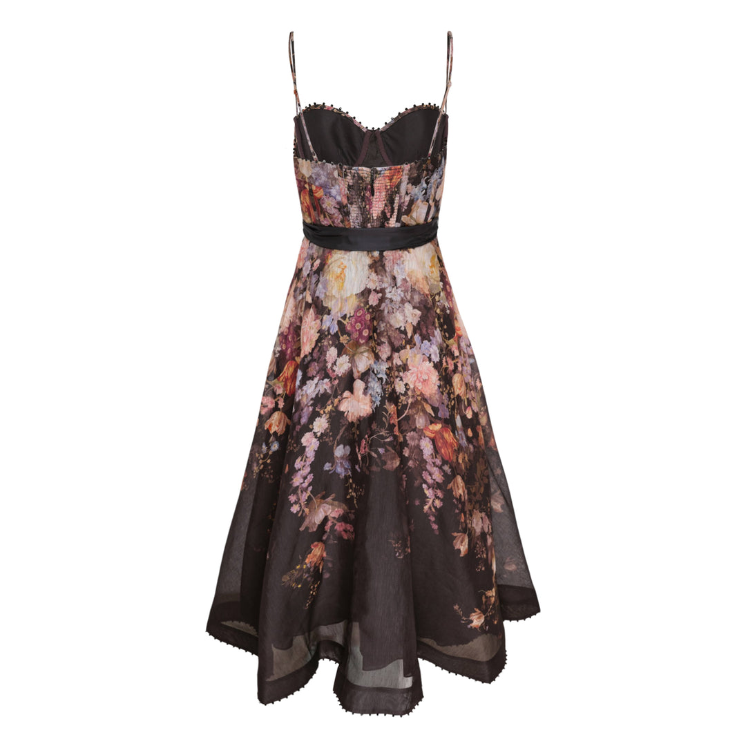 Zimmermann Valiant Corset Picnic Dress in dark botanical floral print, featuring a ruched sweetheart bodice with pom-pom trim, thin spaghetti straps, a branded satin ribbon bow at the waist, and a full semi-sheer A-line midi skirt