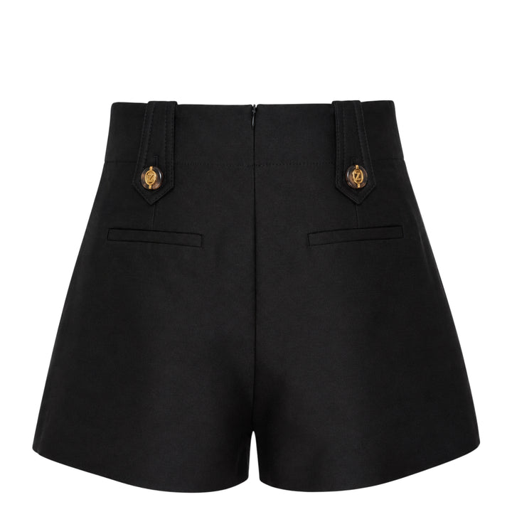 Zimmermann Valiant Tailored Shorts in black with high-rise waistband, A-line silhouette, and signature gold logo button tabs at the waist, shown on a white background