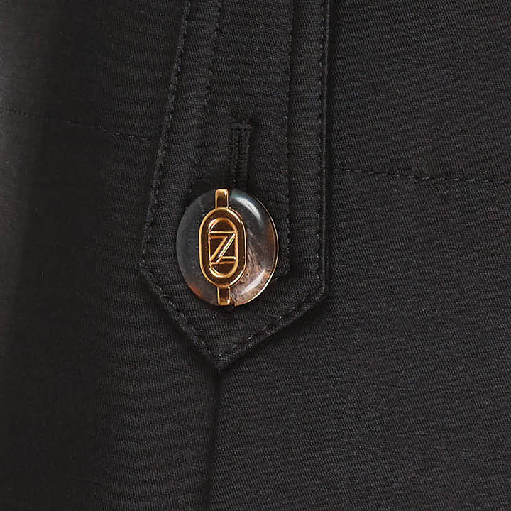 Zimmermann Valiant Tailored Shorts in black with high-rise waistband, A-line silhouette, and signature gold logo button tabs at the waist, shown on a white background