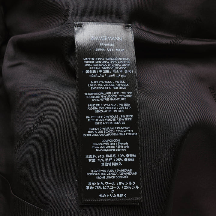 Zimmermann Valiant Tailored Shorts in black with high-rise waistband, A-line silhouette, and signature gold logo button tabs at the waist, shown on a white background