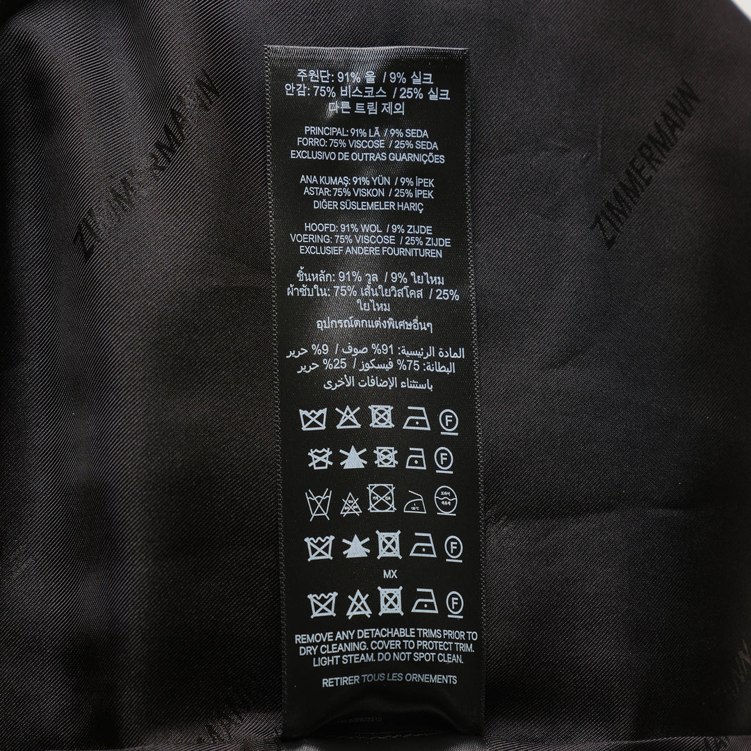 Zimmermann Valiant Tailored Shorts in black with high-rise waistband, A-line silhouette, and signature gold logo button tabs at the waist, shown on a white background