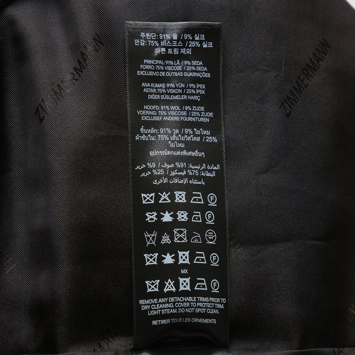 Zimmermann Valiant Tailored Shorts in black with high-rise waistband, A-line silhouette, and signature gold logo button tabs at the waist, shown on a white background