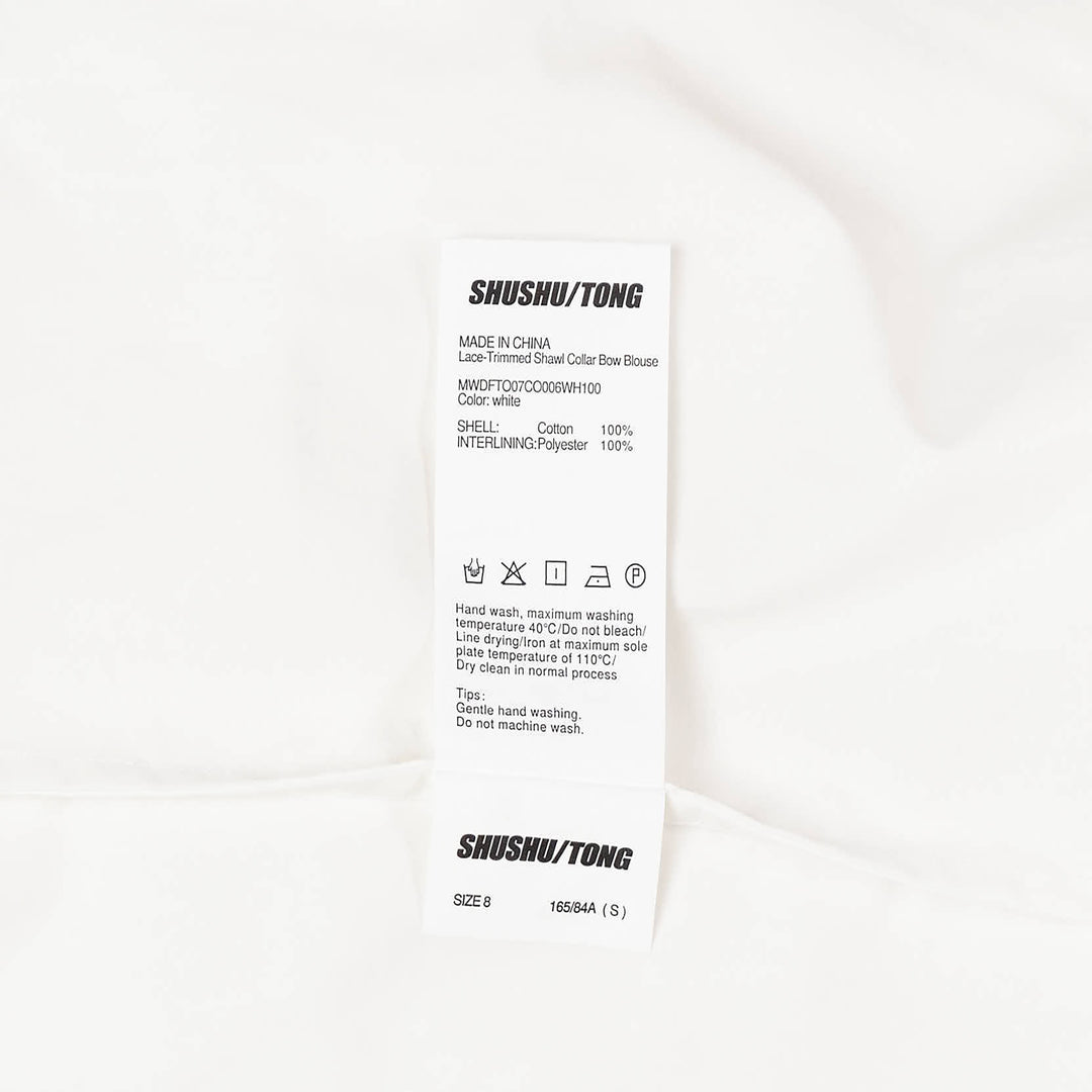 SHUSHU/TONG white sleeveless woven top with ruffled shawl collar and large oversized self-fabric bow at the centre front, photographed against a white background