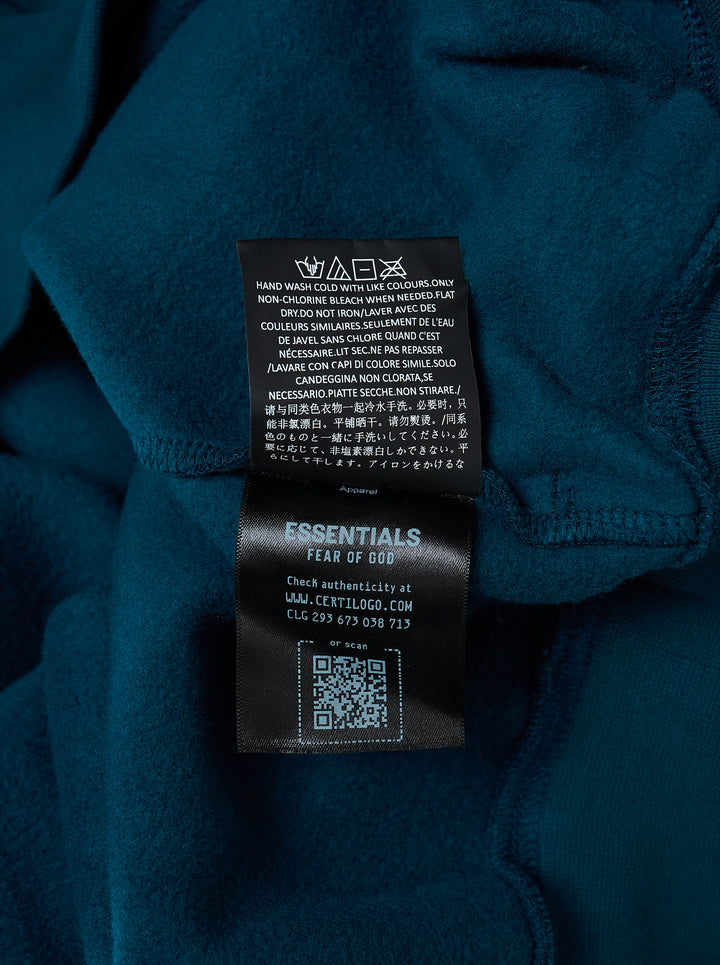 Fear of God Essentials Classic Raglan Hoodie in deep teal with white script logo across the chest and tonal textured shoulder panels - view 4