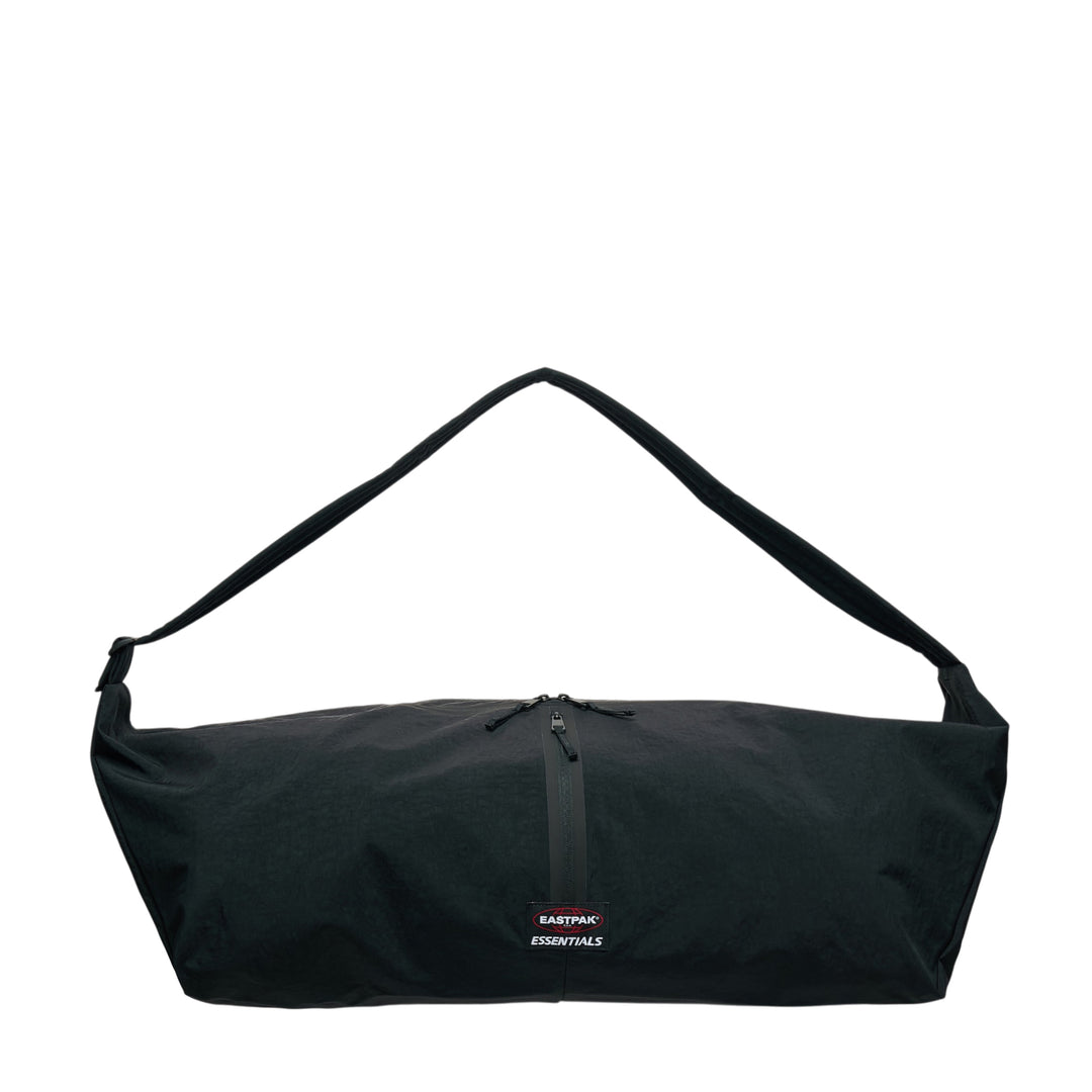 Fear of God ESSENTIALS x Eastpak Shell Bag Large in black, front view showing oversized body, wide shoulder strap, central zip closure, and co-branded woven label