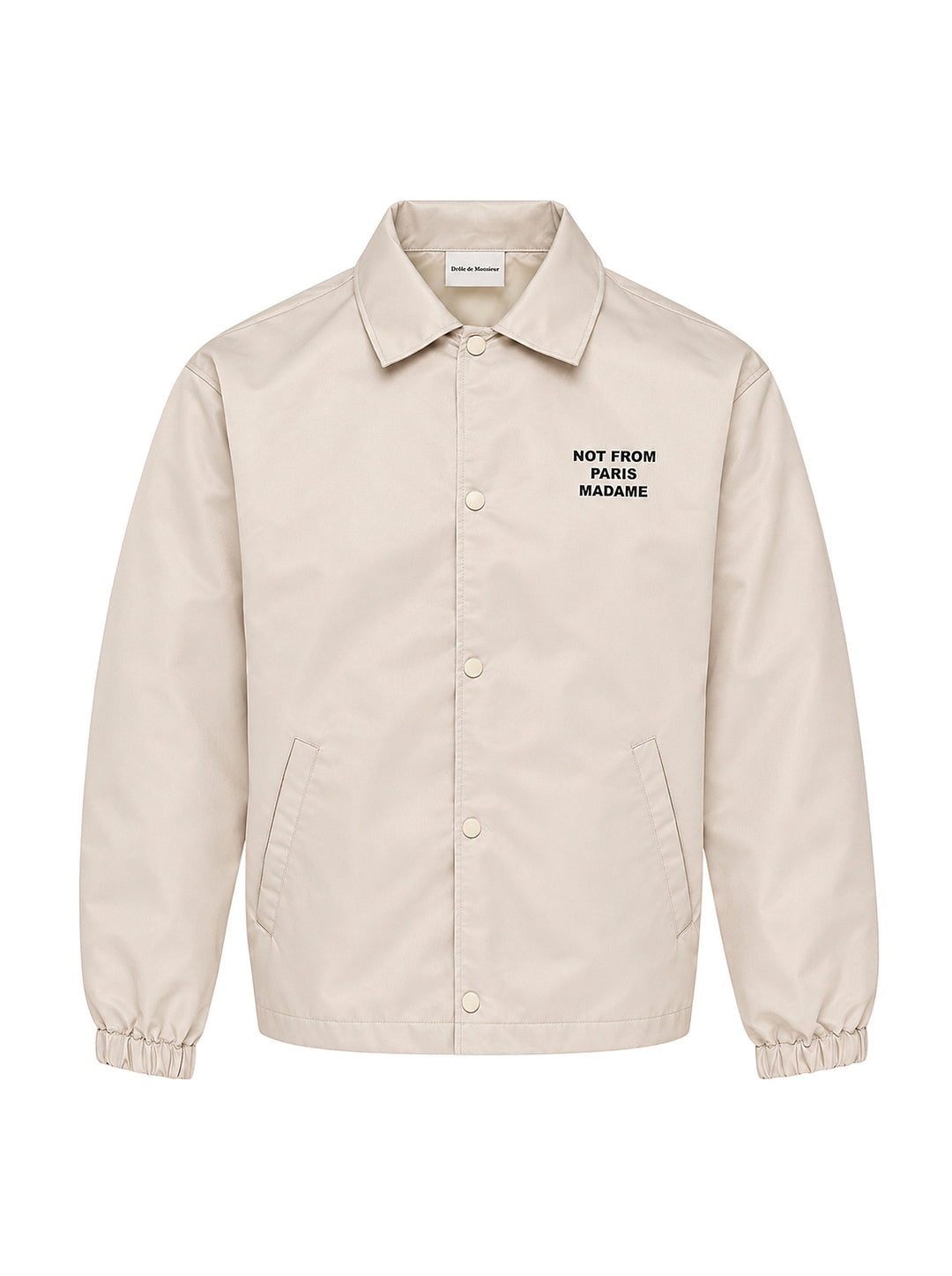 Drôle de Monsieur Not From Paris Madame slogan coach jacket in ecru with snap-button closure, point collar, elasticated cuffs, and embroidered chest slogan